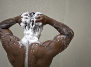 black man with his back to camera shampooing his hair in the shower