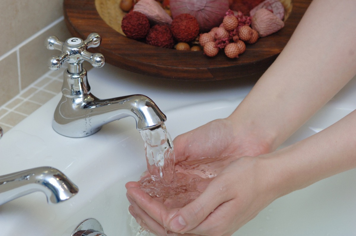 close up of hands under running water in a bathroom sink