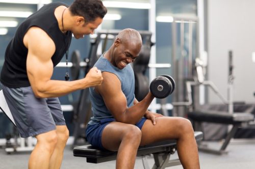 Multicultural men lifting weights in gym helping