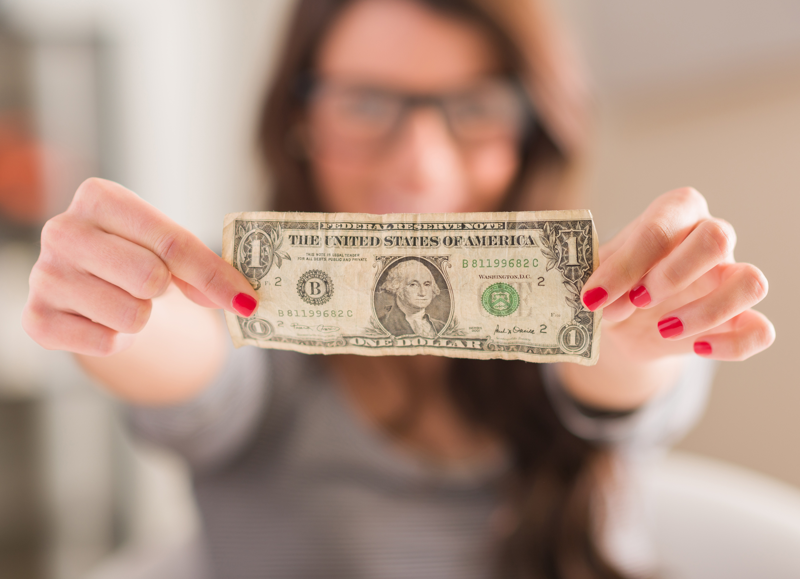 out of focus woman holding up crumpled dollar bill to the camera