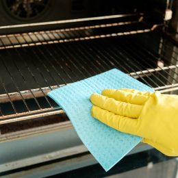 hand in yellow glove cleaning oven with blue sponge