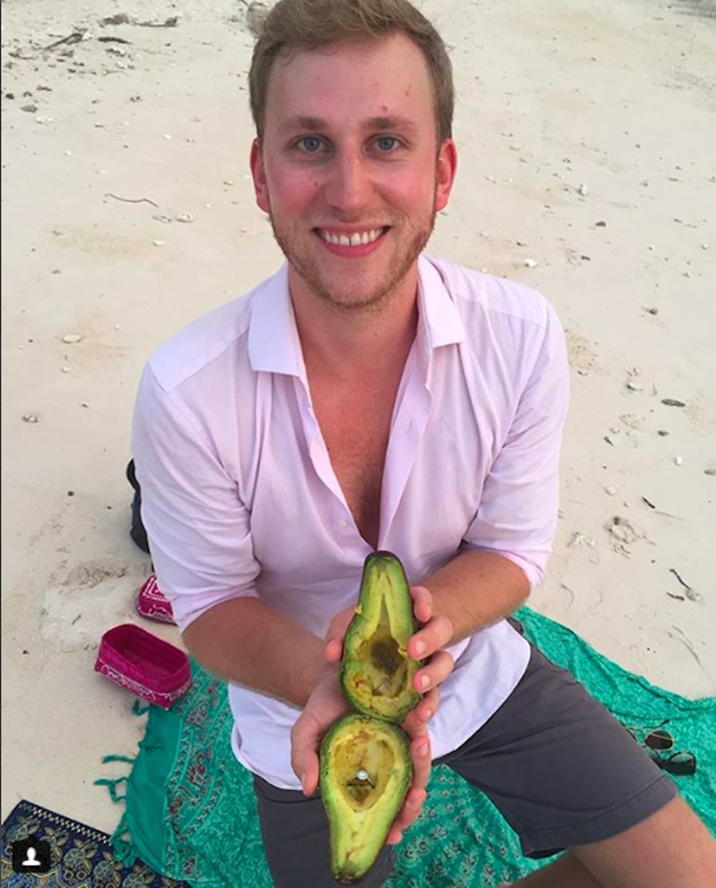 man proposes with avocado on beach.