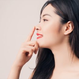 Young beautiful Asian woman with smiley face and red lips touching her nose