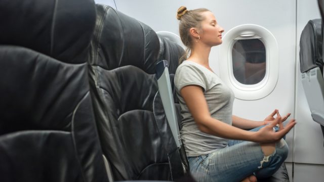 young woman sits in jeans and a gray T-shirt in a black armchair plane. sits in a yoga posture and feels calm