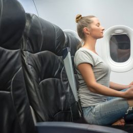 young woman sits in jeans and a gray T-shirt in a black armchair plane. sits in a yoga posture and feels calm