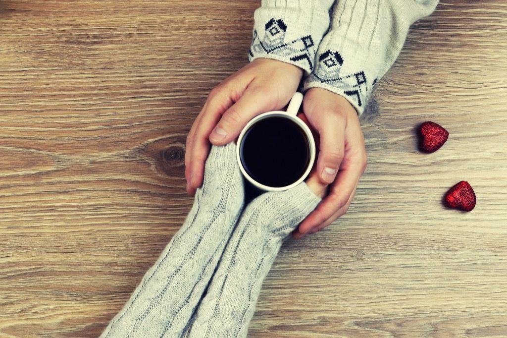 two sets of hands grasp cup of coffee from across a table, photo taken from above