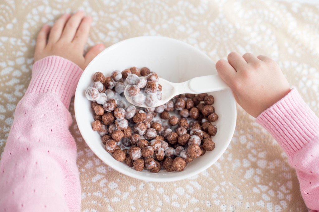 Child eating chocolate cereal from white bowl