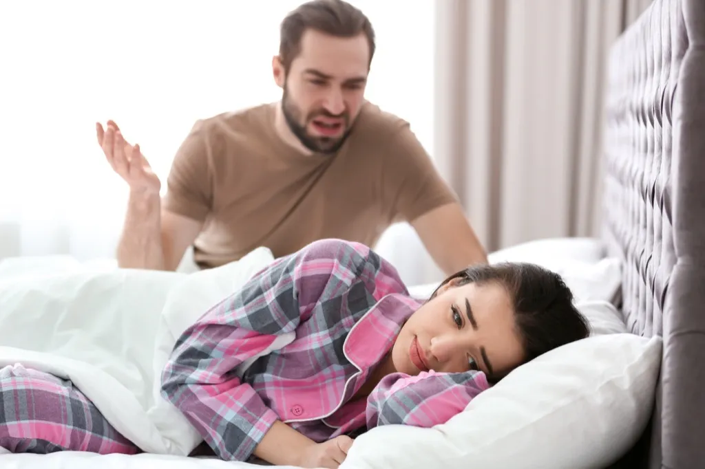 man fighting with crying woman in bed, signs your husband is cheating