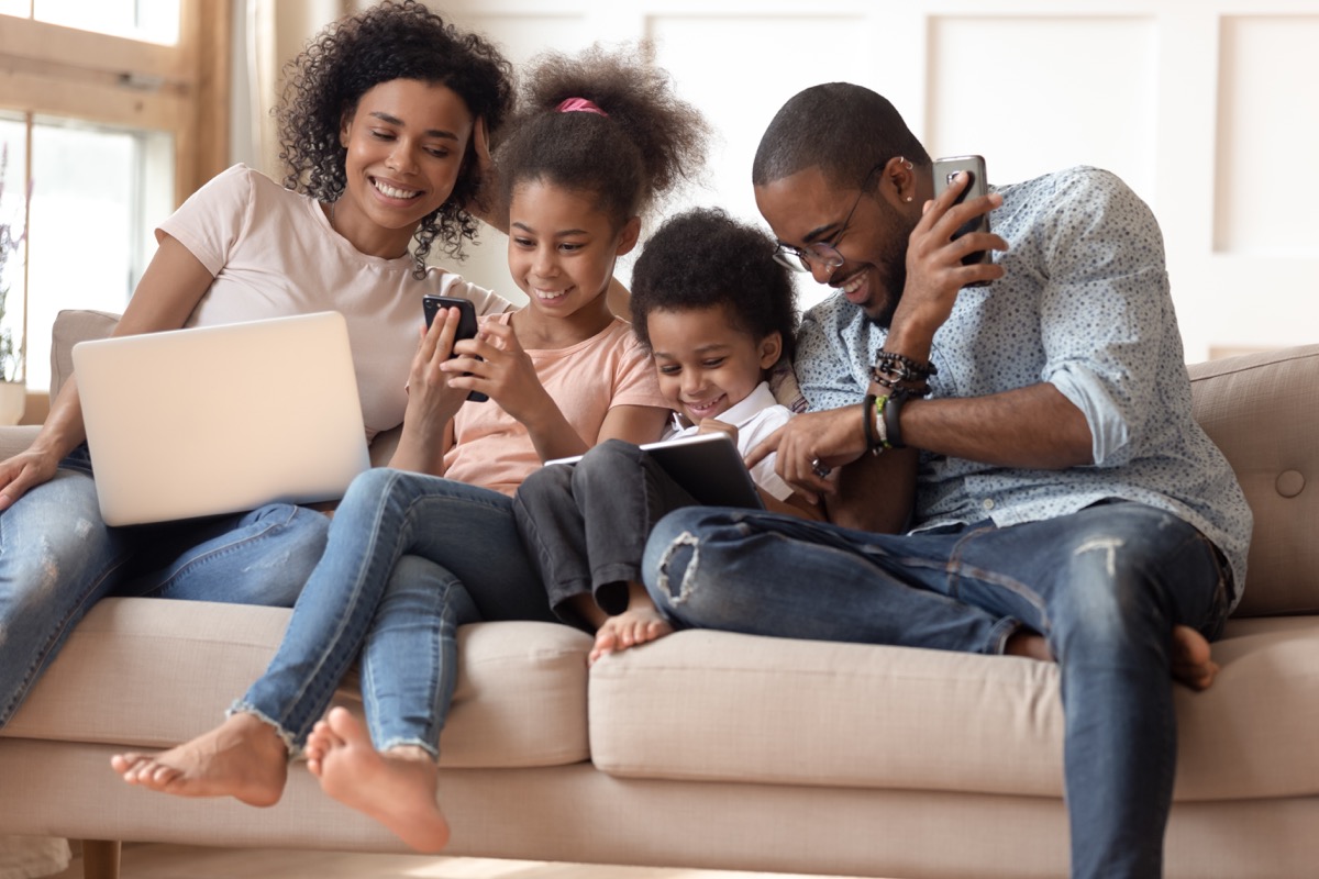 family using various electronic devices on couch