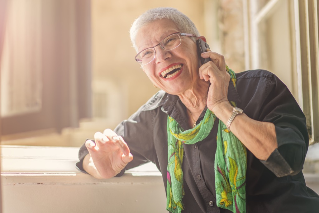 older woman with short grey hair and glasses smiles on phone trying to reach customer service rep