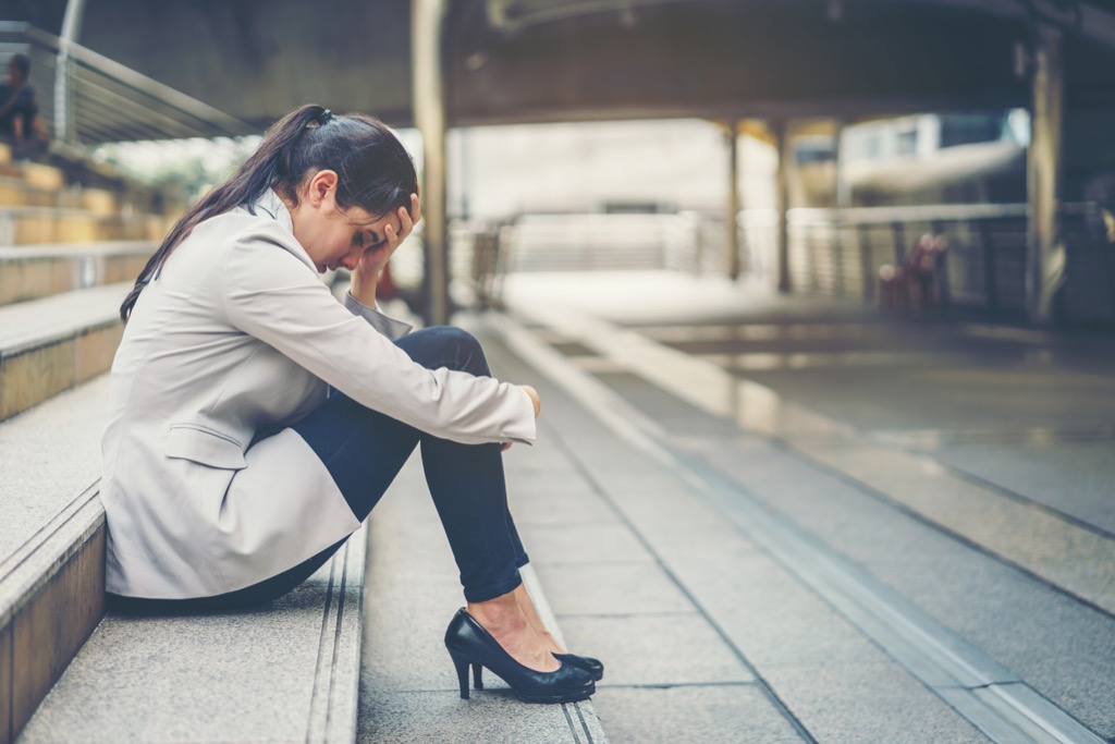 upset woman outside of office on steps holding head in hand