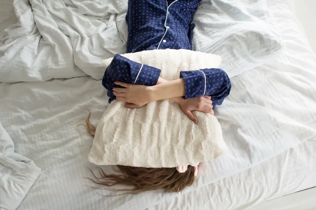 woman in bed covering her face with a pillow