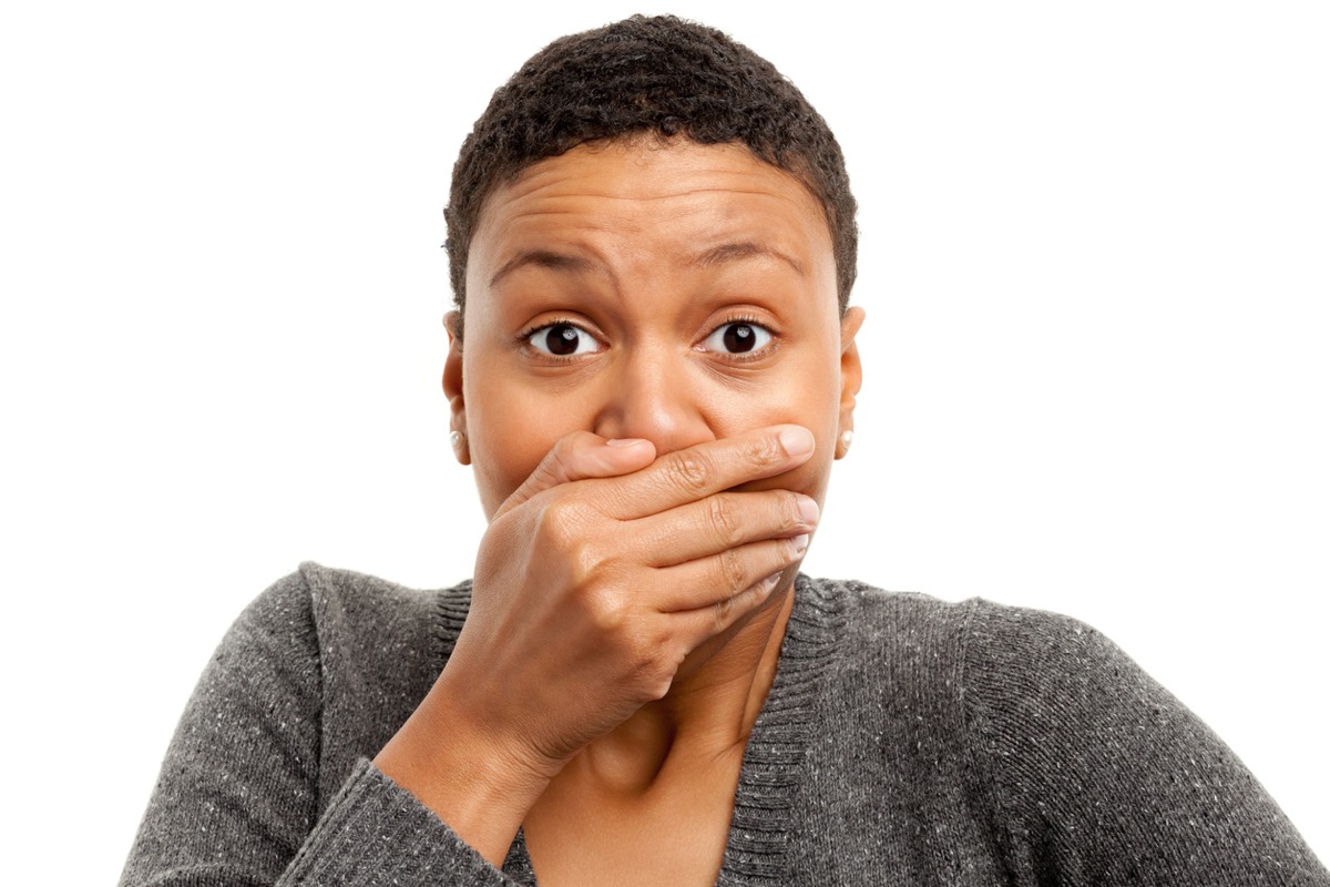 Portrait of a black woman on a white background covering her mouth with her hand