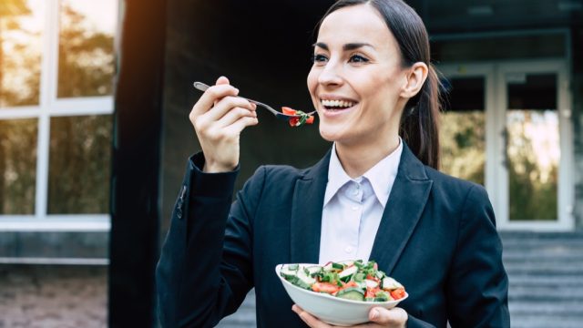 Happy woman eating salad with a fork
