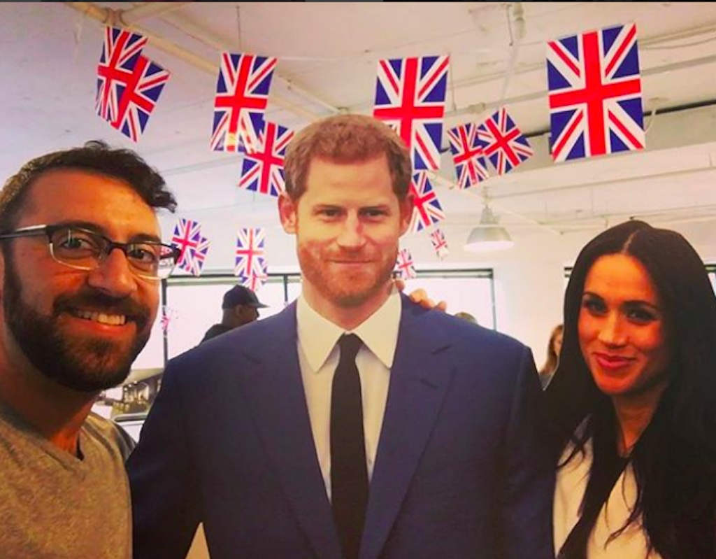 man posing with lifesize cutouts of prince harry and meghan markle. 