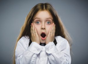 Amazed young girl in white shirt with hands on cheeks looking shocked, childlike wonder facts