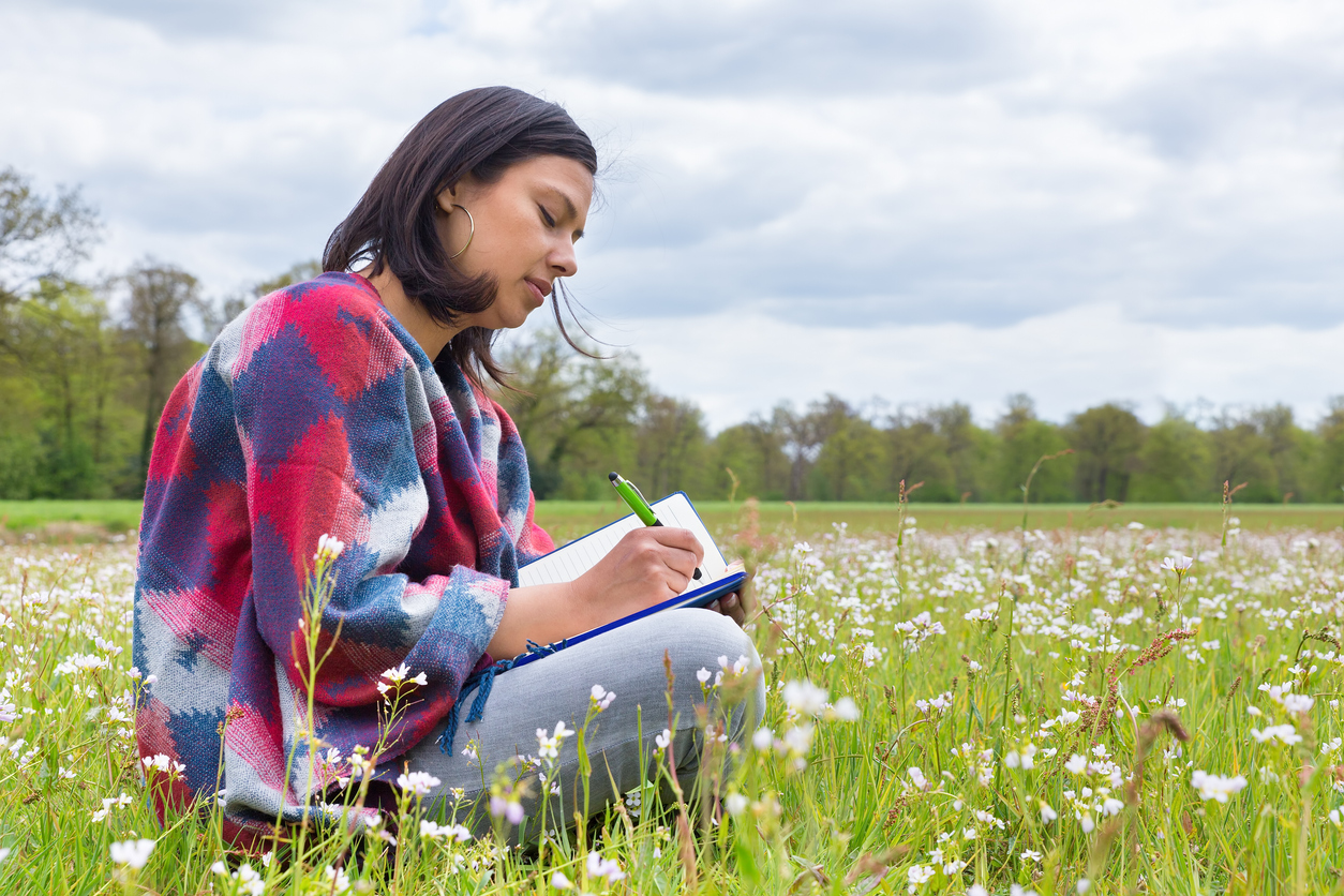 latina woman writing in a journal in a meadow