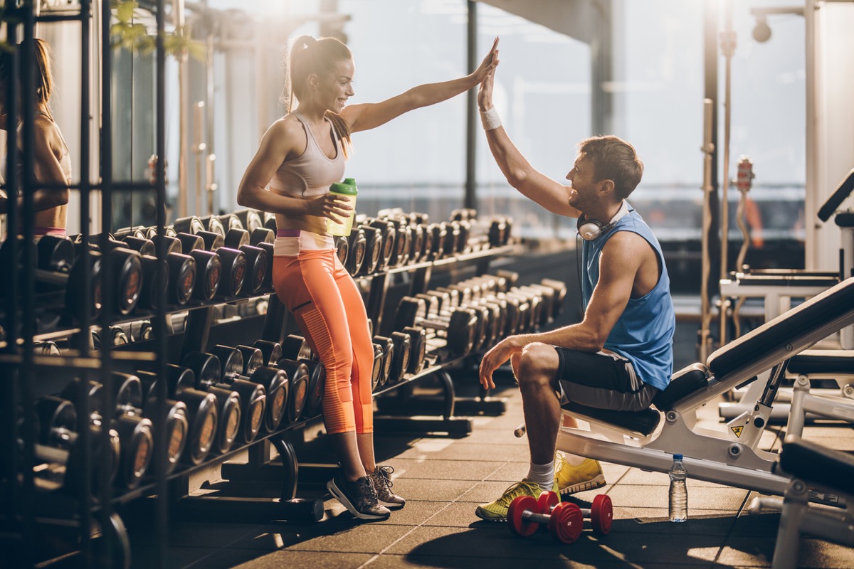 woman and man giving each other a high five by the weights at the gym