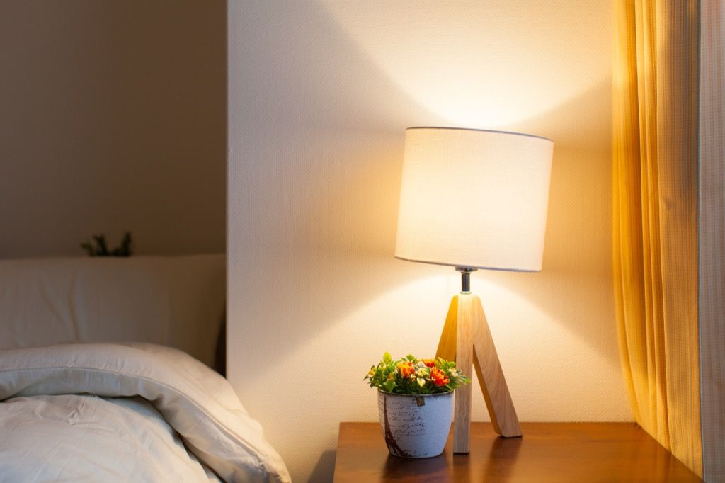 tripod wooden lamp on a wood nightstand next to white bed