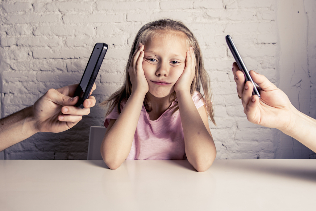 child sulks at parents flip through phones.