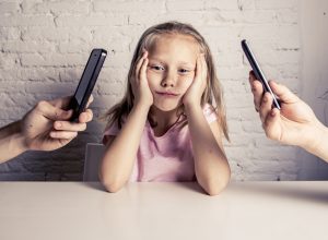 child sulks at parents flip through phones.