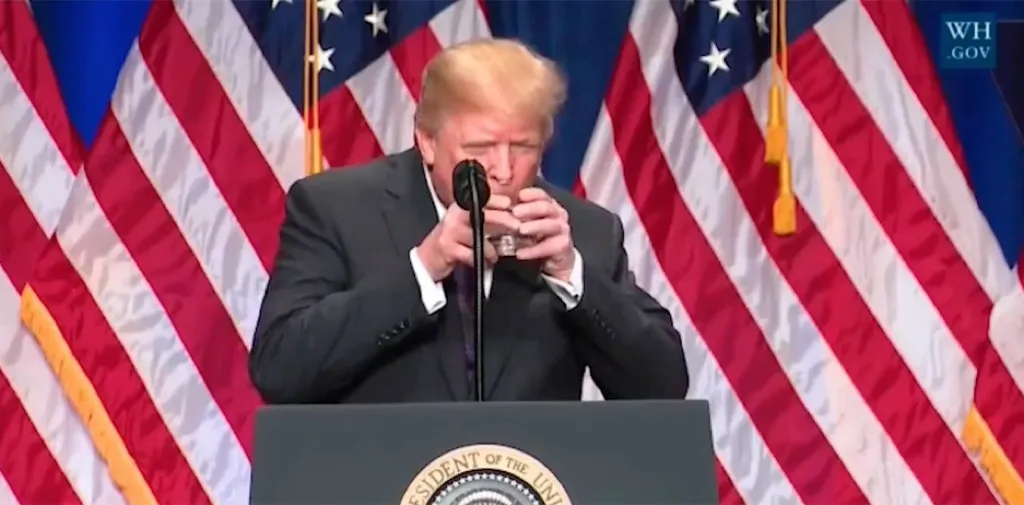 trump uses two hands to hold glass of water