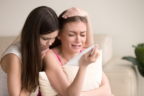 girl crying into pillow with friend hugging her