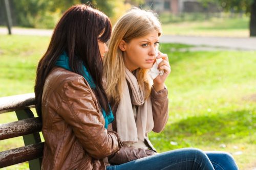 woman comforts crying friend on bench