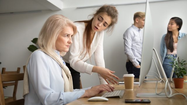 woman looking angry at older coworker on computer