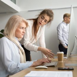 woman looking angry at older coworker on computer