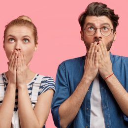 a shocked and surprised hipster couple against a pink background