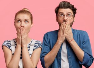a shocked and surprised hipster couple against a pink background