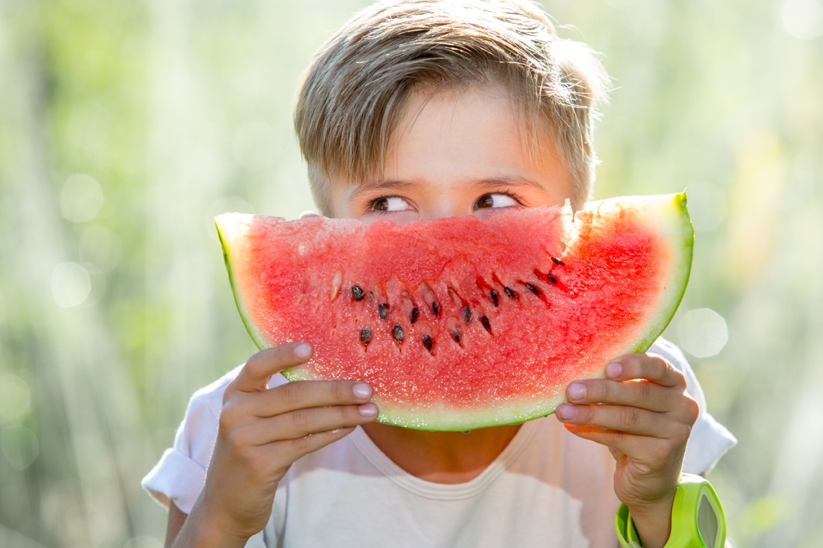kid holding a watermelon in front of his face as if it is a smile
