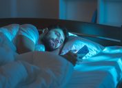 Man is alone in bed reading his phone health tweaks over 40