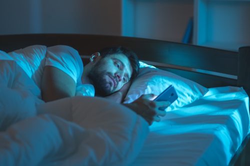 Man is alone in bed reading his phone health tweaks over 40