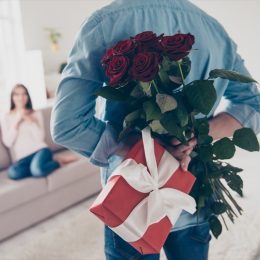 white man holding roses and a gift behind his back