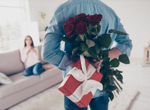 white man holding roses and a gift behind his back