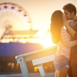 a man and woman kissing in front a ferris wheel
