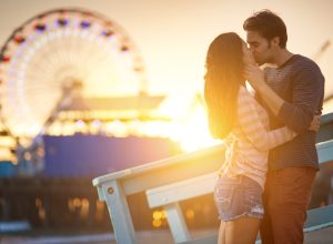 a man and woman kissing in front a ferris wheel