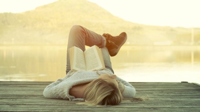 woman relaxing on a dock at sunrise with a book