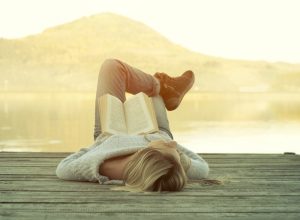 woman relaxing on a dock at sunrise with a book