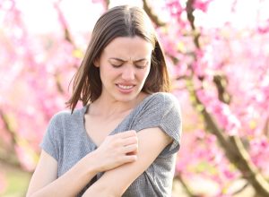 Stressed woman scratching itchy arm after insect bite in a field of peach trees in spring time