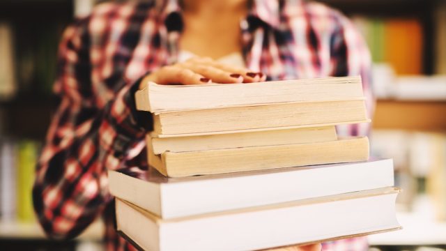 Close up of females hands holding books in front of the camera.