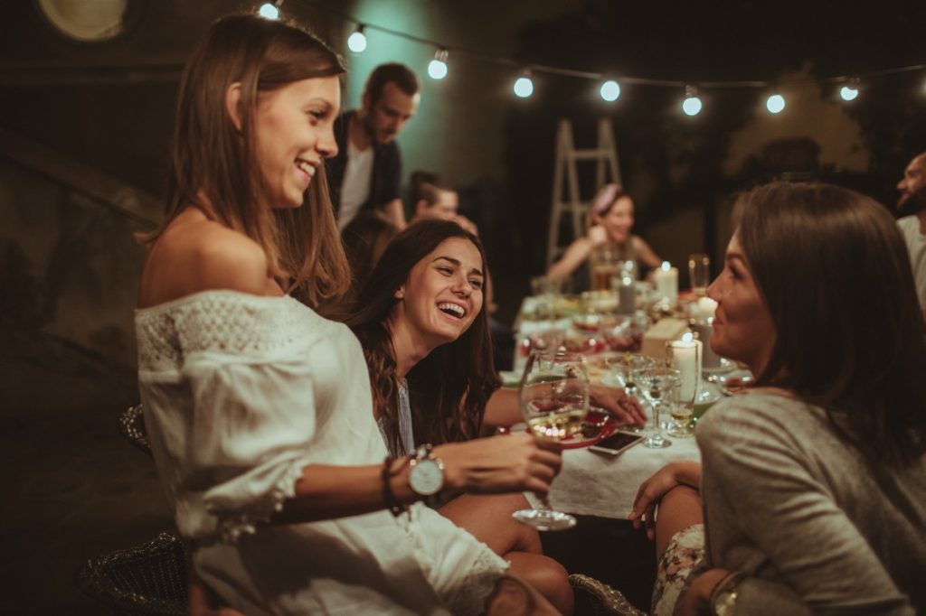 smiling girlfriends at a dinner party with wine