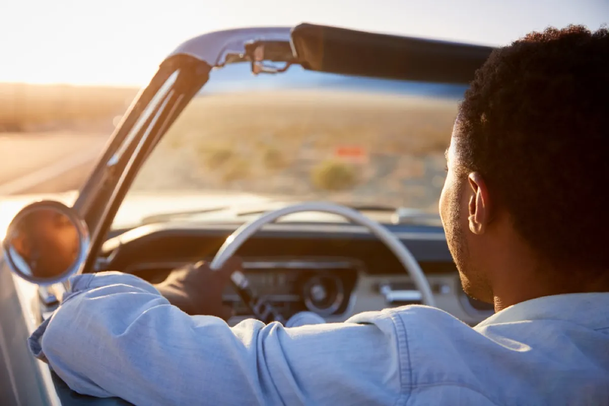 portrait from behind of black man driving a convertible in the desert, changes over 40