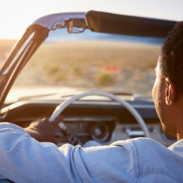portrait from behind of black man driving a convertible in the desert, changes over 40
