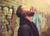 man listening to music on headphones outside in front of a brick wall