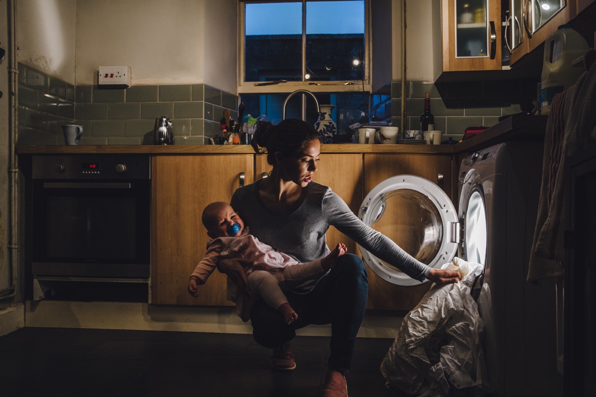 stressed out mother trying to do laundry while holding her baby