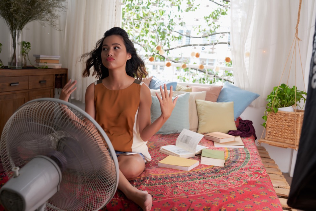 Woman using a fan to cool down in bed, sweating
