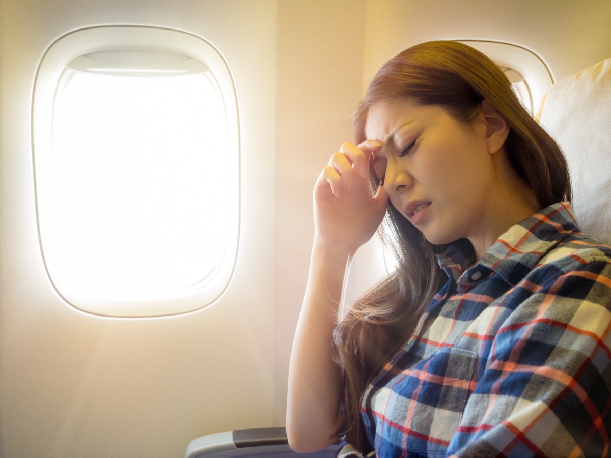 Woman holding her head with a headache on an airplane